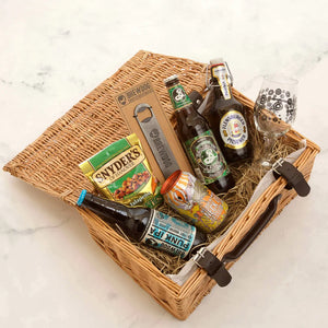 A Fathers Day wicker hamper containing a variety of craft beers, a metal Brewdog bottle opener, a glass, and snacks.