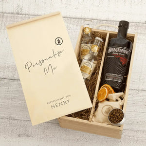 A personalised gift box with two small bottles of tonic water,a black bottle of Brockmans gin, two dried oranges, and a container of spices.