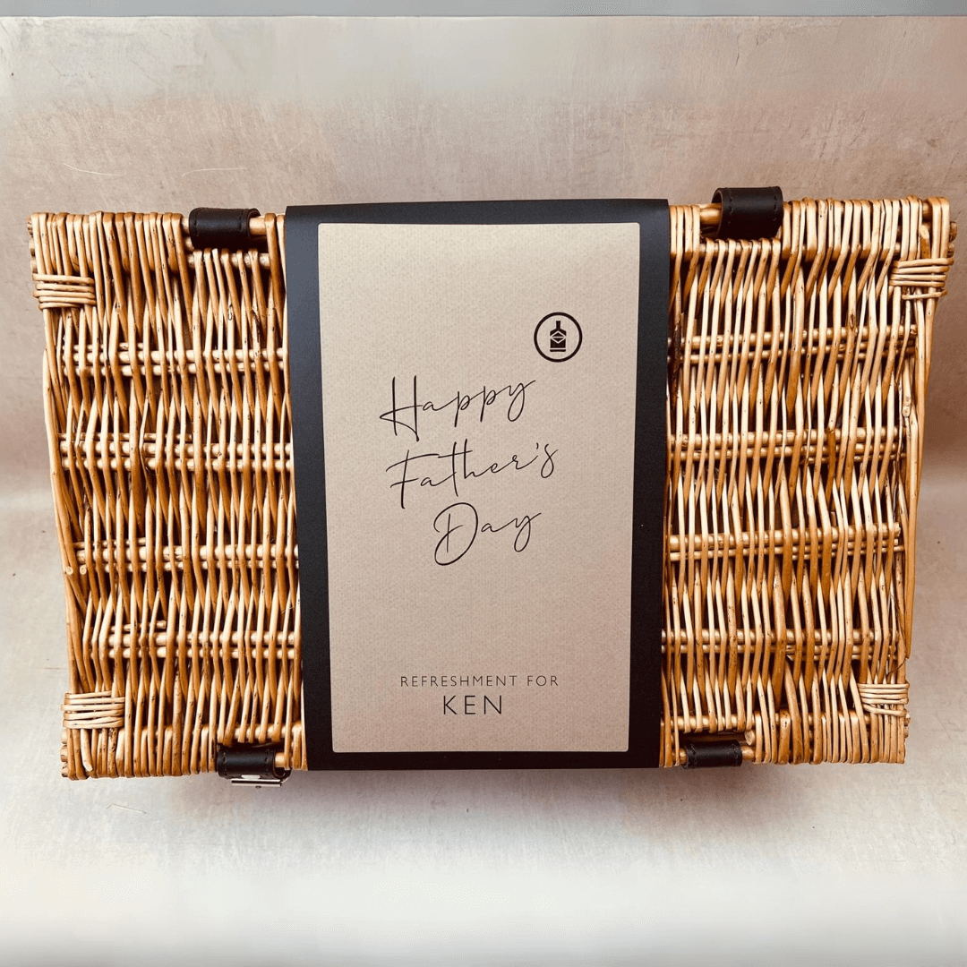 A Father's Day themed gift hamper containing various alcohol-free beers and accompanying snacks, a bottle opener, and a glass, presented in a wicker basket with 'Happy Father's Day' signage.