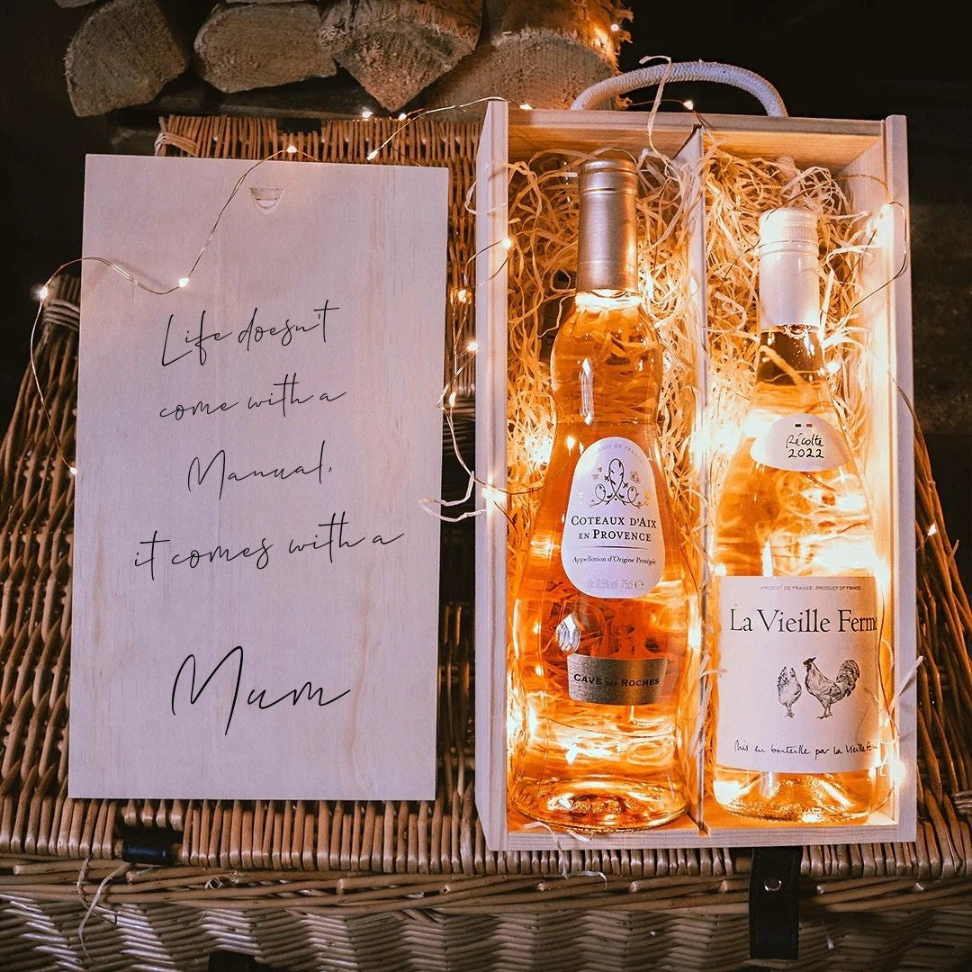 Two bottles of wine in a decorative box with a card reading 'Life doesn't come with a manual, it comes with a mum' on a wooden surface.